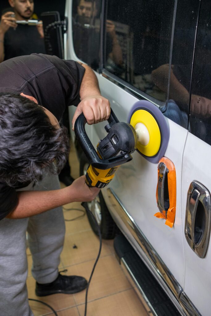 Man polishes car door with electric buffer in auto workshop. Professional detailing service.
